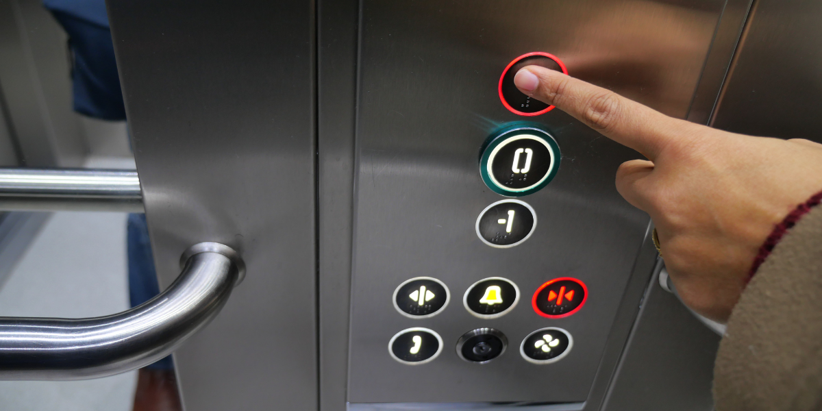 A close-up image of a person's hand in a lift with their finger extended and about to press a button.