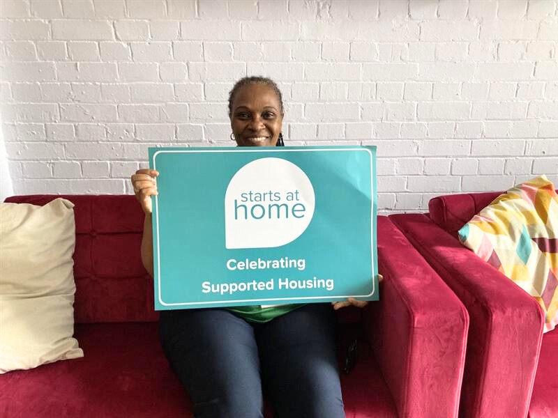 ISHA staff member holds a banner reading, "Support starts at home - celebrating supported housing".