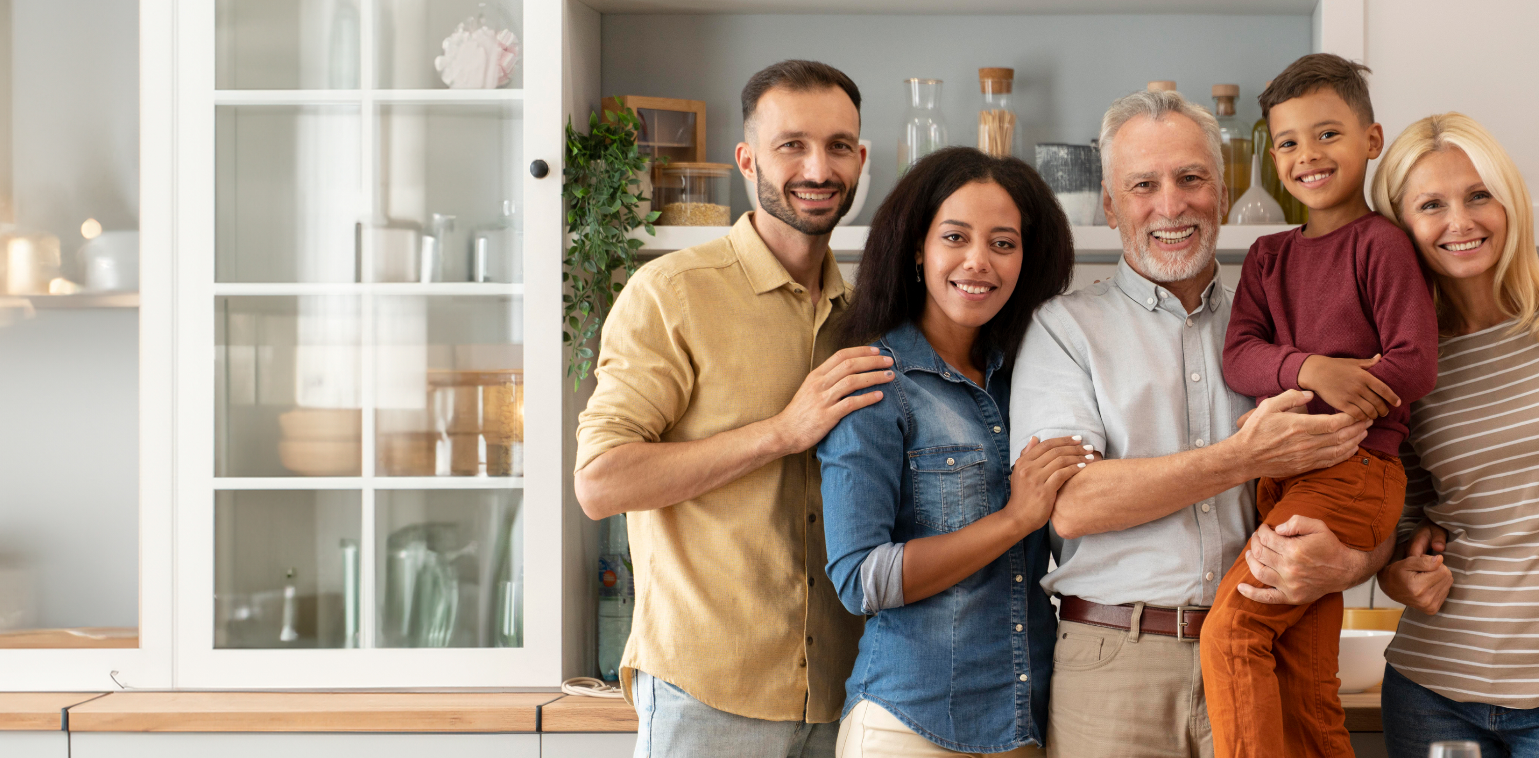 A group of four adults and one child, smiling and standing in a kitchen.